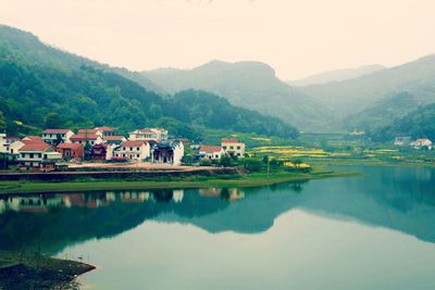 Houses by lake and mountains against sky