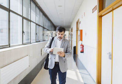 Professor using digital tablet while walking in corridor at university