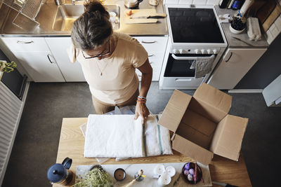 High angle view of woman with disability opening package while standing in kitchen at home