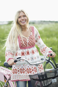 Portrait of happy young woman with bicycle standing on field