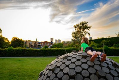 Rear view of boy sitting on grass against sky
