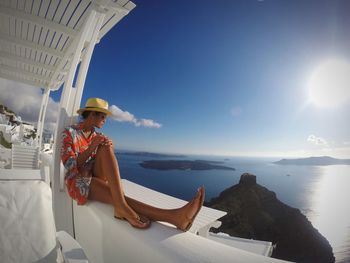 Woman sitting by sea against sky