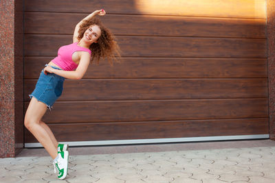 Beautiful curly woman walks in city, against backdrop of brown wall, copy space for text. happy, 