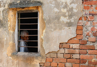 Senior man seen through window on weathered brick wall