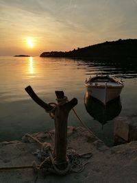 Boat moored on sea against sky during sunset