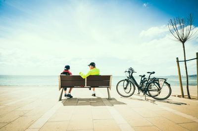 Rear view of men sitting on bicycle by sea against sky