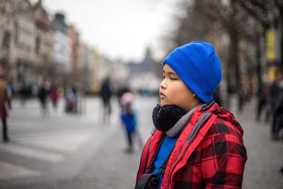 Side view of boy in knit hat and jacket standing on city street