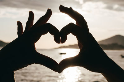 Heart shape with hand against sky during sunset
