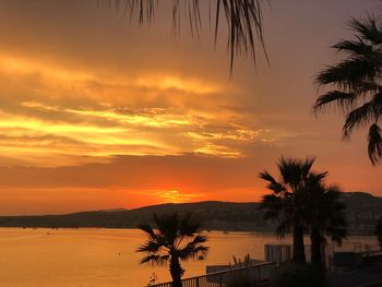 Silhouette palm trees by sea against romantic sky at sunset