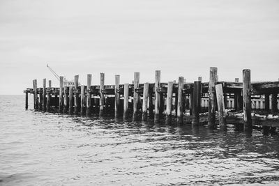 Wooden posts in sea against clear sky