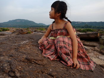 Beautiful young woman sitting on land against mountains