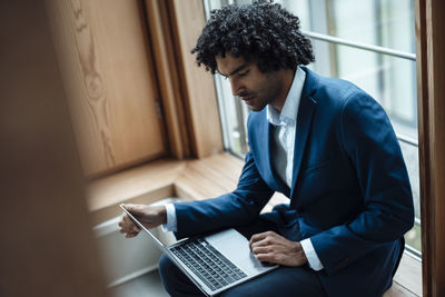 Young male professional using laptop while sitting against window at office