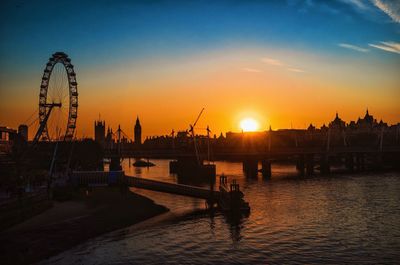 Silhouette millennium wheel and big ben by thames river against orange sky