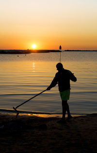 Silhouette man fishing at beach against sky during sunset