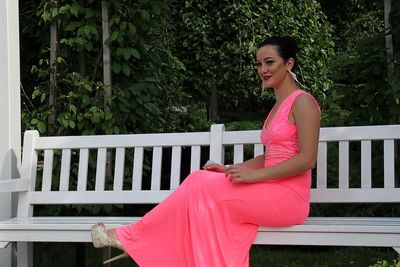 Side view of smiling young woman sitting on bench in garden