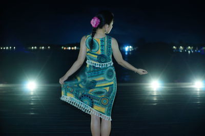 Woman on illuminated lighting equipment at night