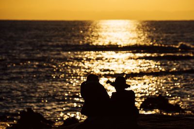 Silhouette couple at beach against sky during sunset