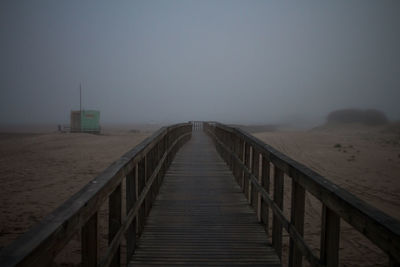 Wooden footbridge over land against sky