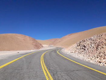 Road leading towards mountain against clear blue sky