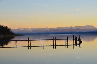 Wooden posts in lake against sky during sunset