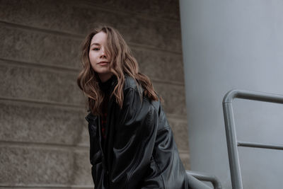 Young woman looking down while sitting on staircase against wall