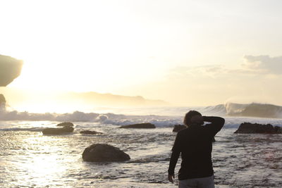 Rear view of woman looking at sea against sky during sunset