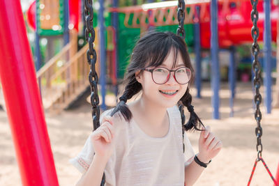 Portrait of smiling young woman sitting on swing at playground