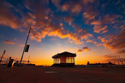 Silhouette building by street against sky during sunset