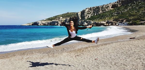 Woman with arms raised and legs apart jumping at beach during sunny day