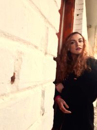 Portrait of young woman standing against wall