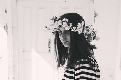 Portrait of young woman wearing flowers standing against door