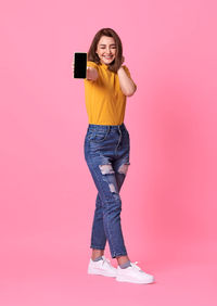 Full length of happy woman standing against pink background