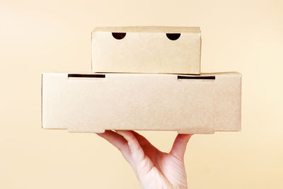 Female hand holds two cardboard boxes with food on a brown background.