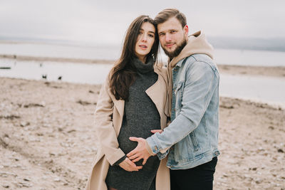 Portrait of man standing with pregnant woman at beach