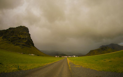 Empty road along landscape against cloudy sky