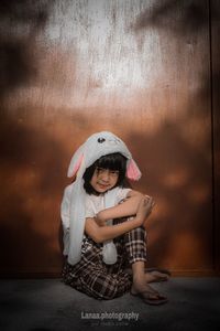 Portrait of cute girl sitting against wall