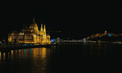 Illuminated buildings by river against sky at night