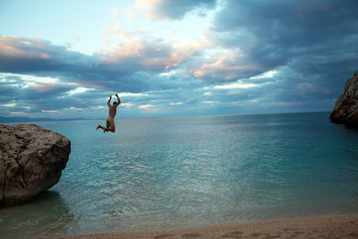 Naked man jumping into sea against sky during sunset