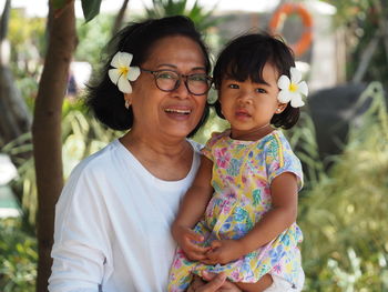 An asian grandmother wearing frangipani flower in her ear while holding her adorable grandchild