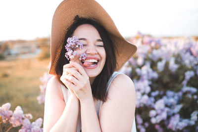 Happy beautiful young woman having fun hold lilac flower wear straw hat over nature meadow outdoors.