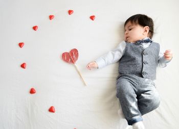 High angle view of cute baby by heart shape candy on bed at home