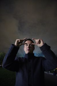 Thoughtful man gesturing against cloudy sky at night