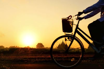 Silhouette man riding bicycle on street during sunset
