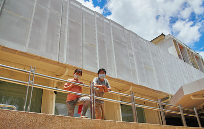 Low angle view of men standing on railing against building