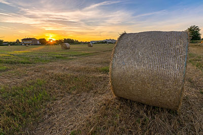 Hay bales on field against sky during sunset