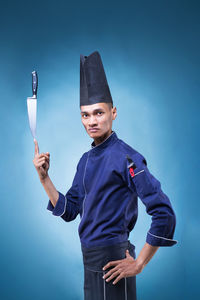 Portrait of chef balancing knife on finger against blue background