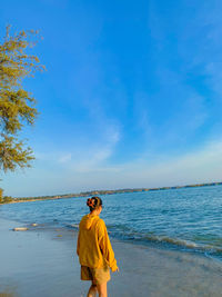 Rear view of woman standing at beach against sky