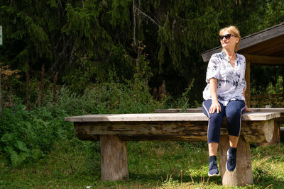 Full length of woman sitting on wooden bench outdoors