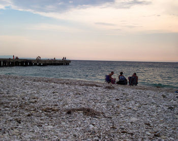 People sitting on beach against sky during sunset