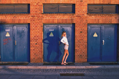 Side view of young woman standing against door of building